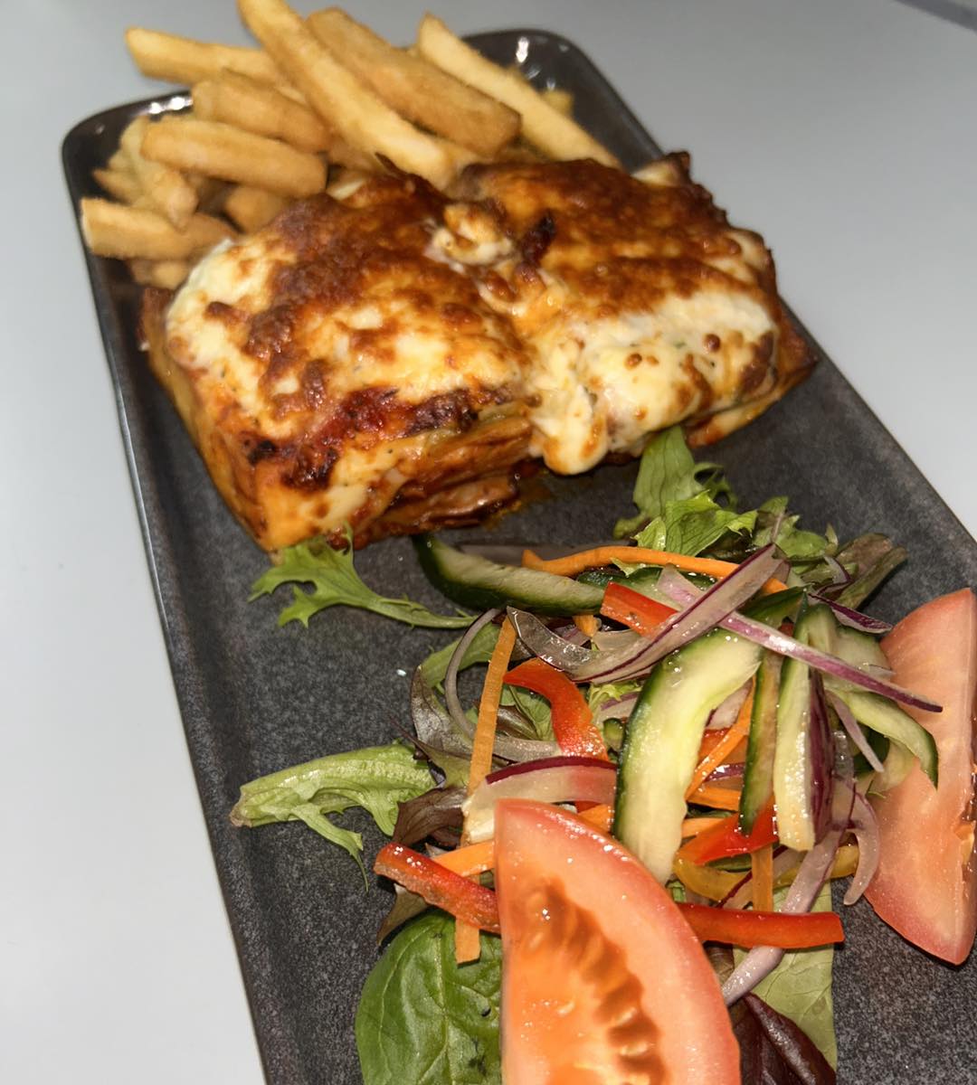 Golden cheese-topped baked dish served with chips and a fresh garden salad