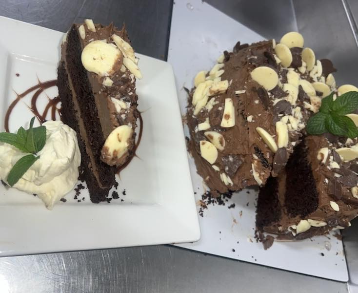 Chocolate cake with white chocolate buttons, sliced and served with cream and mint