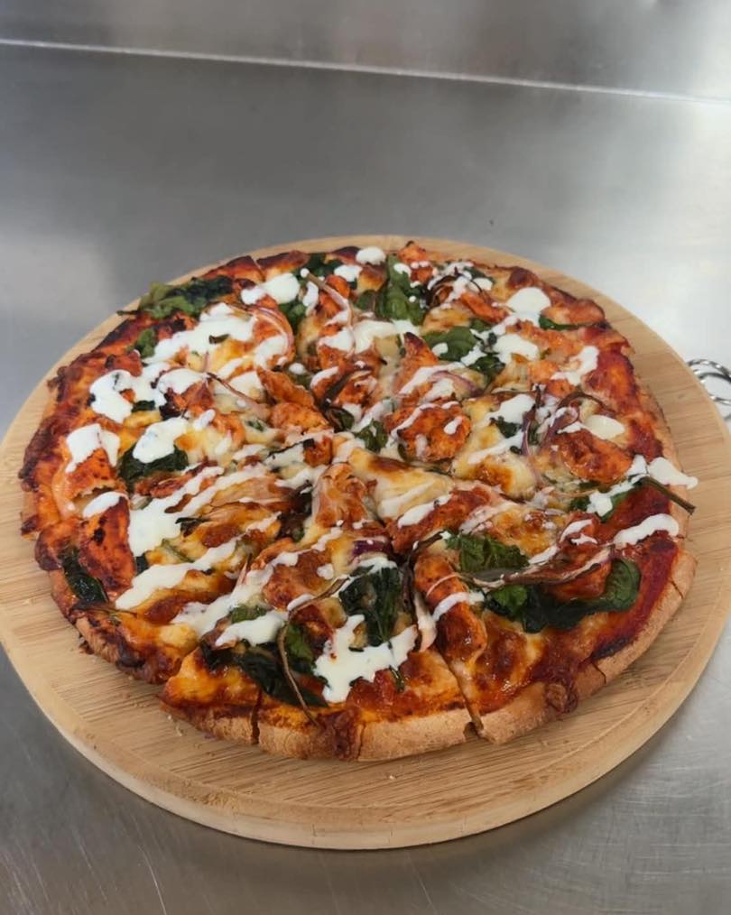 Pizza with sauce drizzle and spinach on a round wooden board