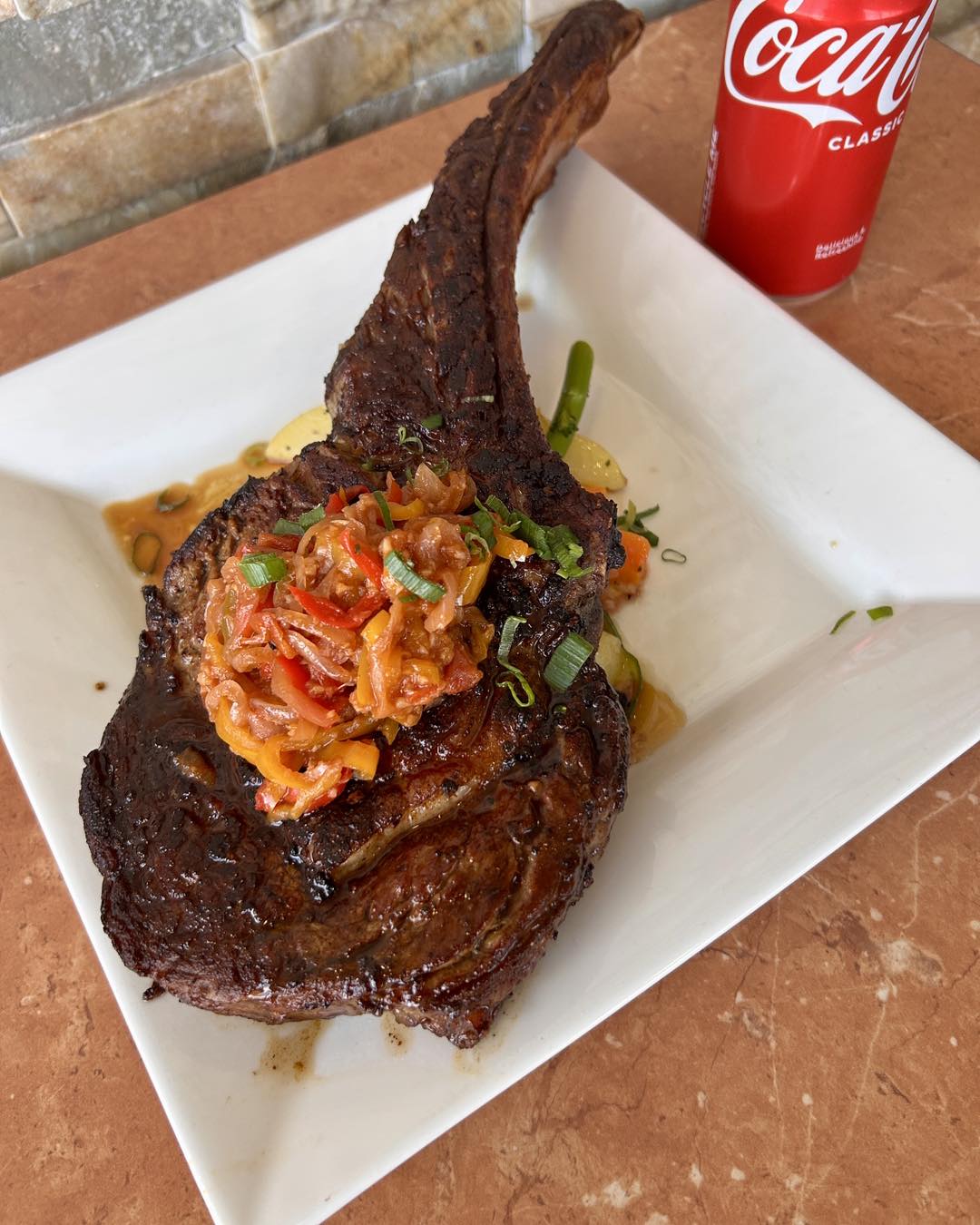 Seared tomahawk-style steak topped with capsicum relish on a square white plate